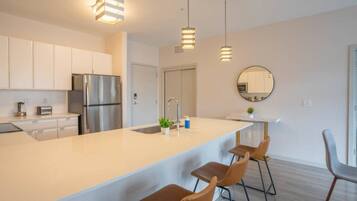 Una cocina moderna con electrodomésticos de acero inoxidable, una isla grande con taburetes de bar, iluminación colgante y un espejo redondo en la pared.