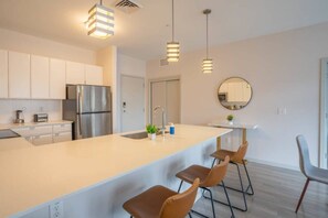 A modern kitchen with stainless steel appliances, a large island with bar stools, pendant lighting, and a round mirror on the wall. - Downtown Phoenix Retreat | Walk to Arts District (Phoenix)