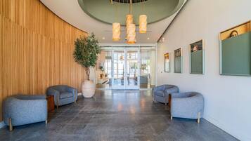 A modern lobby with a curved ceiling, two grey sofas, a large potted plant, and a reception desk.