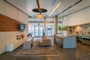 A modern hotel lobby with a seating area, a bar, and a kitchen visible through the glass doors. - Arts Downtown PHX | Pool, Gym, Balcony & Parking (Phoenix)
