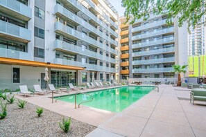 A modern apartment building with a swimming pool, outdoor seating, and a covered area with umbrellas. - Arts Downtown PHX | Pool, Gym, Balcony & Parking (Phoenix)