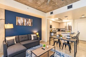 A modern living room with a sofa, coffee table, and a dining area with chairs and a table. - Arts Downtown PHX | Pool, Gym, Balcony & Parking (Phoenix)