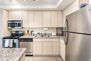 A modern kitchen with stainless steel appliances, a granite countertop, and light wood cabinetry. - Arts Downtown PHX | Pool, Gym, Balcony & Parking (Phoenix)
