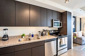 Une cuisine moderne avec des meubles de couleur sombre, des appareils électroménagers en acier inoxydable et un plan de travail en granit.
