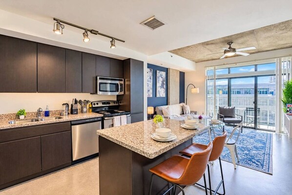 A modern kitchen with dark cabinetry, stainless steel appliances, and a granite countertop.