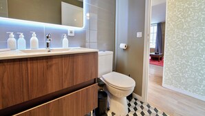 A modern bathroom with a wooden vanity, a white toilet, and a large mirror with integrated lighting. - Le Petit Appartement du 10honfleur, Calme, Quartier Ste Catherine (Honfleur)