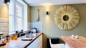 A modern kitchen with a wooden countertop, a sink, and a black dishwasher. There is a large decorative mirror on the wall and a white chair near the counter. - Le Petit Appartement du 10honfleur, Calme, Quartier Ste Catherine (Honfleur)