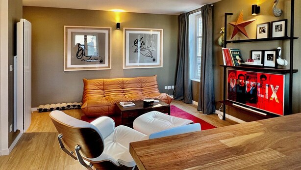A modern living room with a sofa, coffee table, and TV stand. There are framed pictures on the wall and a bookshelf with books and decorative items. - Le Petit Appartement du 10honfleur, Calme, Quartier Ste Catherine (Honfleur)