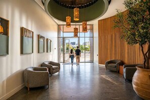 Un hall d’entrée moderne avec un plafond incurvé, des luminaires suspendus et un grand mur recouvert de panneaux en bois.