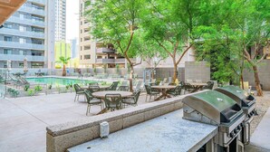 An outdoor patio with a pool, grilling stations, and seating areas surrounded by trees.