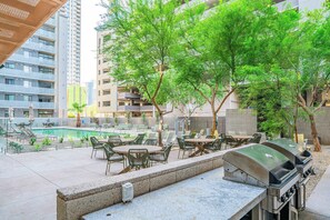 Un patio al aire libre con piscina, estaciones de parrillada y zonas de estar rodeado de árboles.