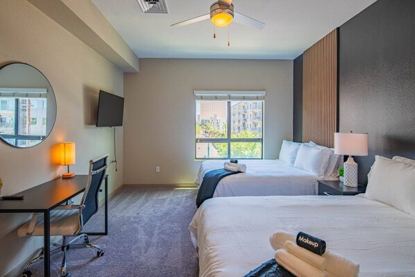 A hotel room with a bed, desk, chair, lamp, and a ceiling fan.