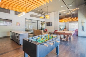 A modern indoor space with a foosball table, a pool table, and a kitchen area.