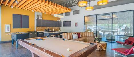 Ein Billardtisch, ein Tischfußballspiel und eine Couch in einem modernen Lounge-Bereich mit großen Fenstern.