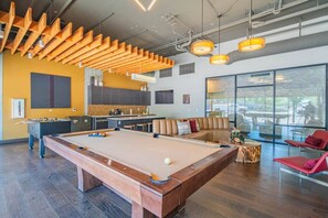 A pool table with a foosball table and a sofa in a modern lounge area with large windows.