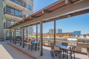 An outdoor patio area with tables and chairs, a grill, and a view of the city skyline.