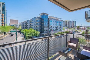 En balkon med fletmøbler med udsigt over en bygning og moderne bygninger.