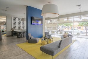 Un hall d’hôtel moderne avec un canapé, des fauteuils, un téléviseur et une grande fenêtre donnant sur la rue.