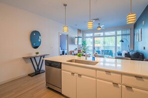 Cocina moderna con isla central, lavavajillas integrado, iluminación colgante y vistas a un balcón.