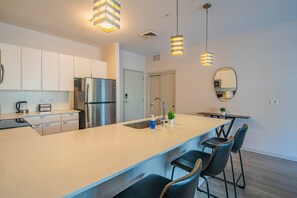 Une cuisine moderne dotée d’un îlot central, d’appareils électroménagers en acier inoxydable, de luminaires suspendus et d’un coin repas avec des tabourets de bar.