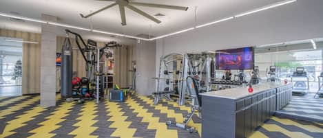 Un gimnasio con equipo de ejercicio, una banca de pesas central y una pantalla de televisión grande.