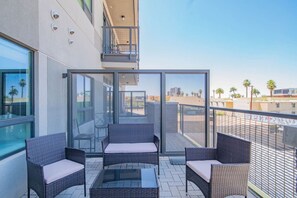 Een balkon met rieten meubels en een glazen tafel, met uitzicht op een stadsgezicht met palmbomen.