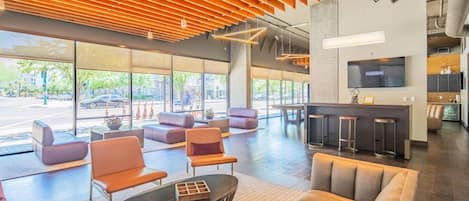 A spacious lobby with a modern design, featuring a bar area, seating arrangements, and large windows providing natural light.