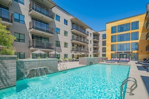 A modern building with a swimming pool, outdoor seating, and a waterfall feature.