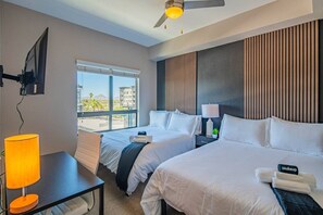 A hotel room with two beds, a desk, a lamp, and a view of the city.