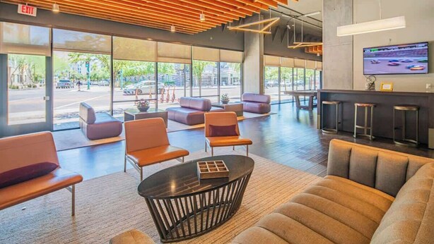 A spacious lobby with modern seating, large windows, and a television screen.