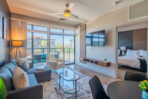 A modern hotel room with a sofa, armchair, and a TV mounted on the wall.