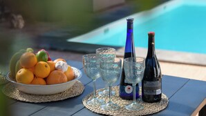 A table with a bowl of fruit, wine glasses, and bottles, near a pool. - Boutique Boho Glam Villa With Private Pool (Yaiza)