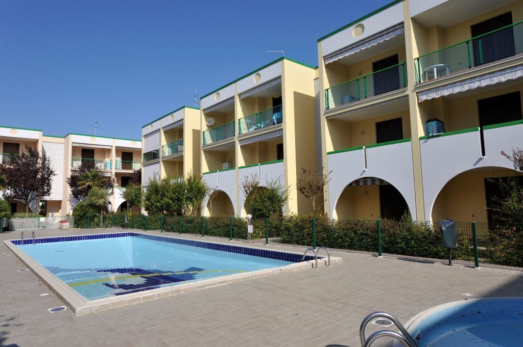 A swimming pool adjacent to a multi-story hotel with balconies and arched windows.