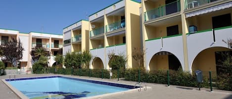 A swimming pool adjacent to a multi-story hotel with balconies and arched windows.
