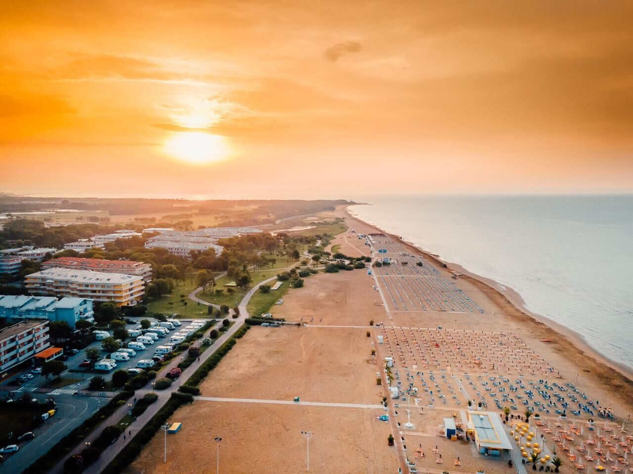 An aerial view of a beach with a parking lot and buildings in the background.