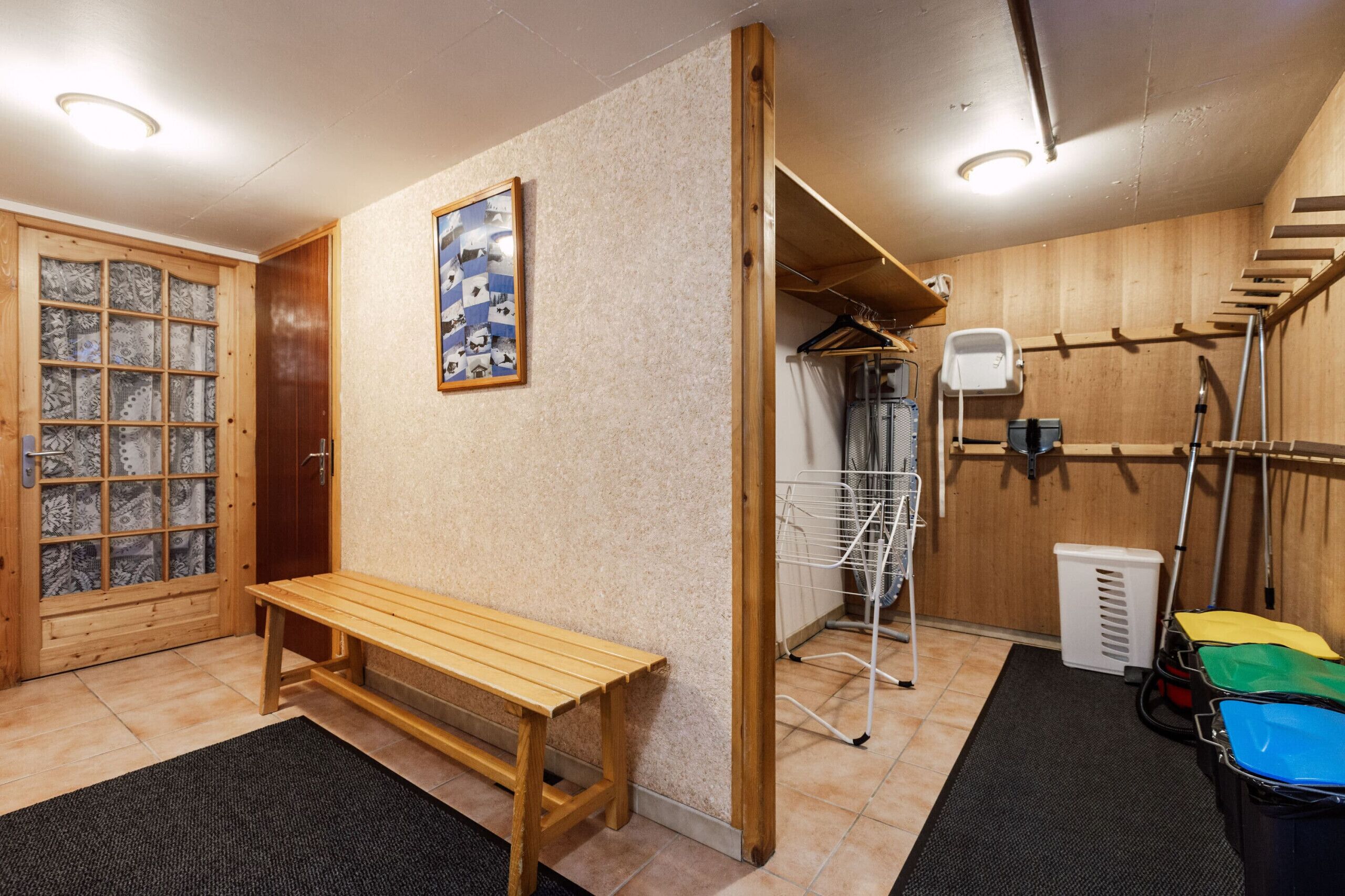 Une pièce comprenant un banc en bois, une porte en bois avec des panneaux de verre, un tableau accroché au mur, un étendoir et un escalier.