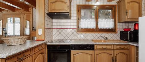 Una cocina con armarios de madera, un lavavajillas Bosch, un fregadero y una ventana con cortina de encaje.