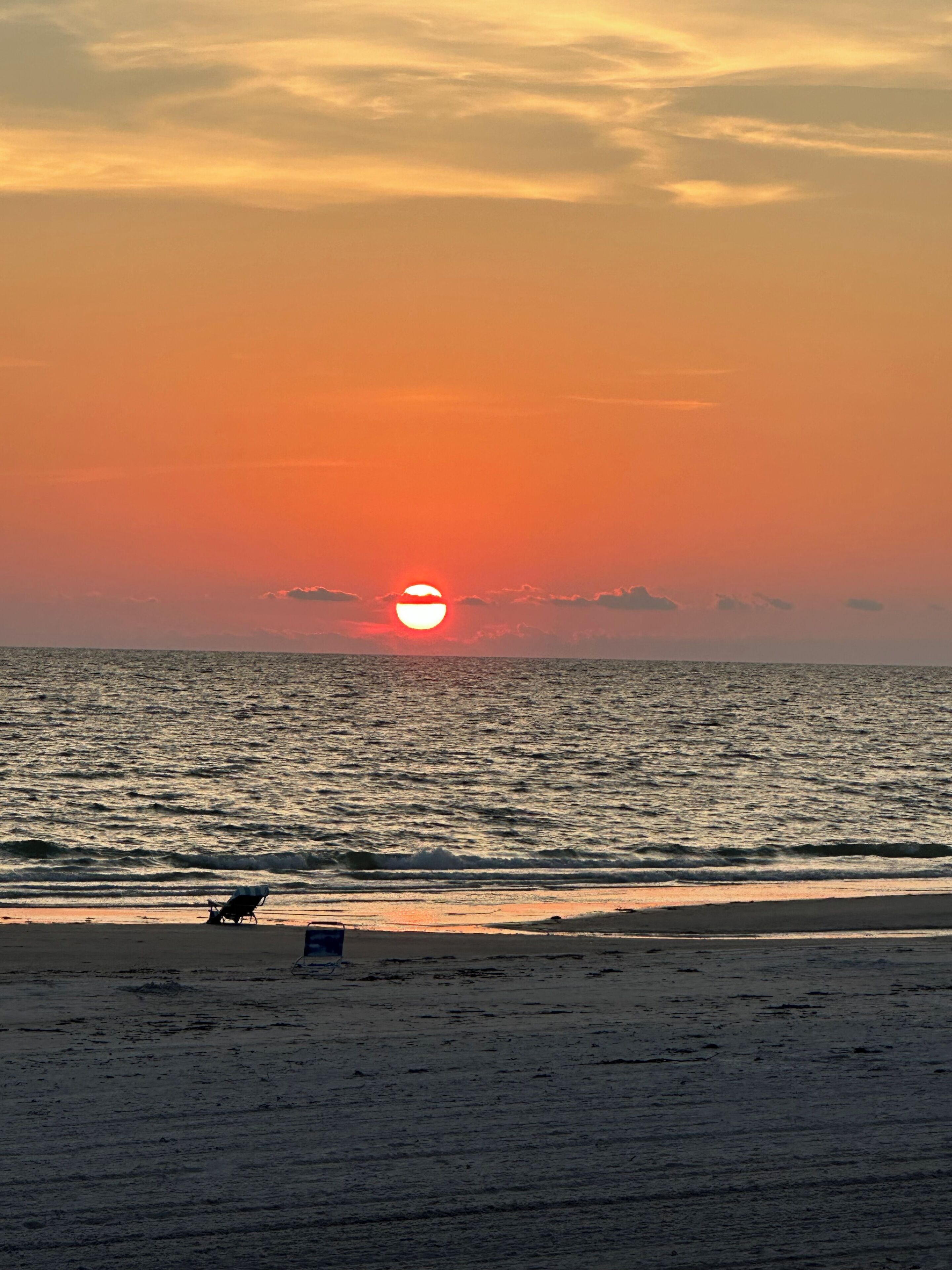Une scène de plage au coucher du soleil, avec des vagues sur l’océan et une personne assise sur une chaise de plage.
