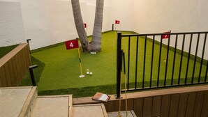 Un parcours de mini-golf avec des trous numérotés, un banc en bois et une rambarde.