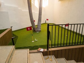 Un camp de mini golf amb forats numerats, una banca de fusta i una barana.
