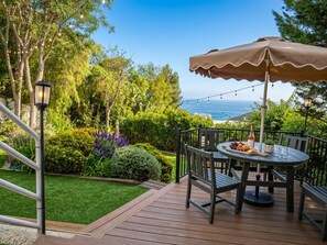 Een terras met een tafel en stoelen, een zonnescherm en uitzicht op de oceaan.