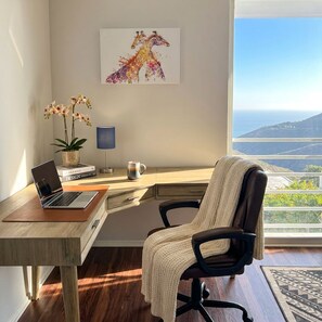 Een moderne kantoorruimte met een bureau, laptop en uitzicht op een kustlandschap.
