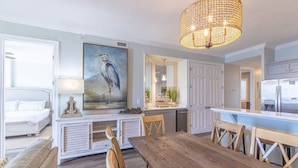 Un vaste espace de vie comprenant une table à manger en bois, un grand tableau et, au fond, une cuisine moderne.