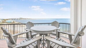 Un balcon avec une table ronde et quatre chaises Adirondack, donnant sur une plage et l’océan.