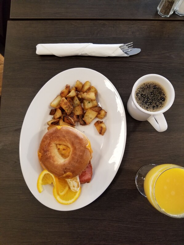 A breakfast plate with a sausage roll, fried potatoes, and a glass of orange juice on a wooden table. - Mansfield Outdoor Centre (Mulmur)