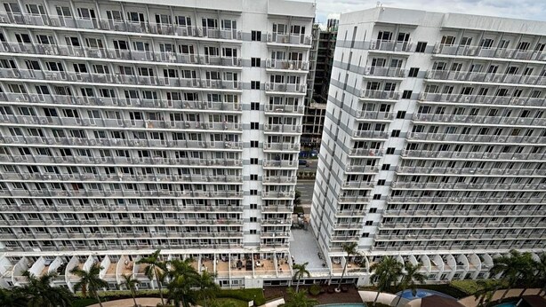 A high-rise hotel with multiple balconies and a large, multi-level swimming pool area. - Apartment hotel in front of biggest mall of asia with resort type amenity pool.  (Pasay)