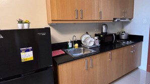 A compact kitchen with wooden cabinets, a black refrigerator, a sink, and a kettle. - Apartment hotel in front of biggest mall of asia with resort type amenity pool.  (Pasay)
