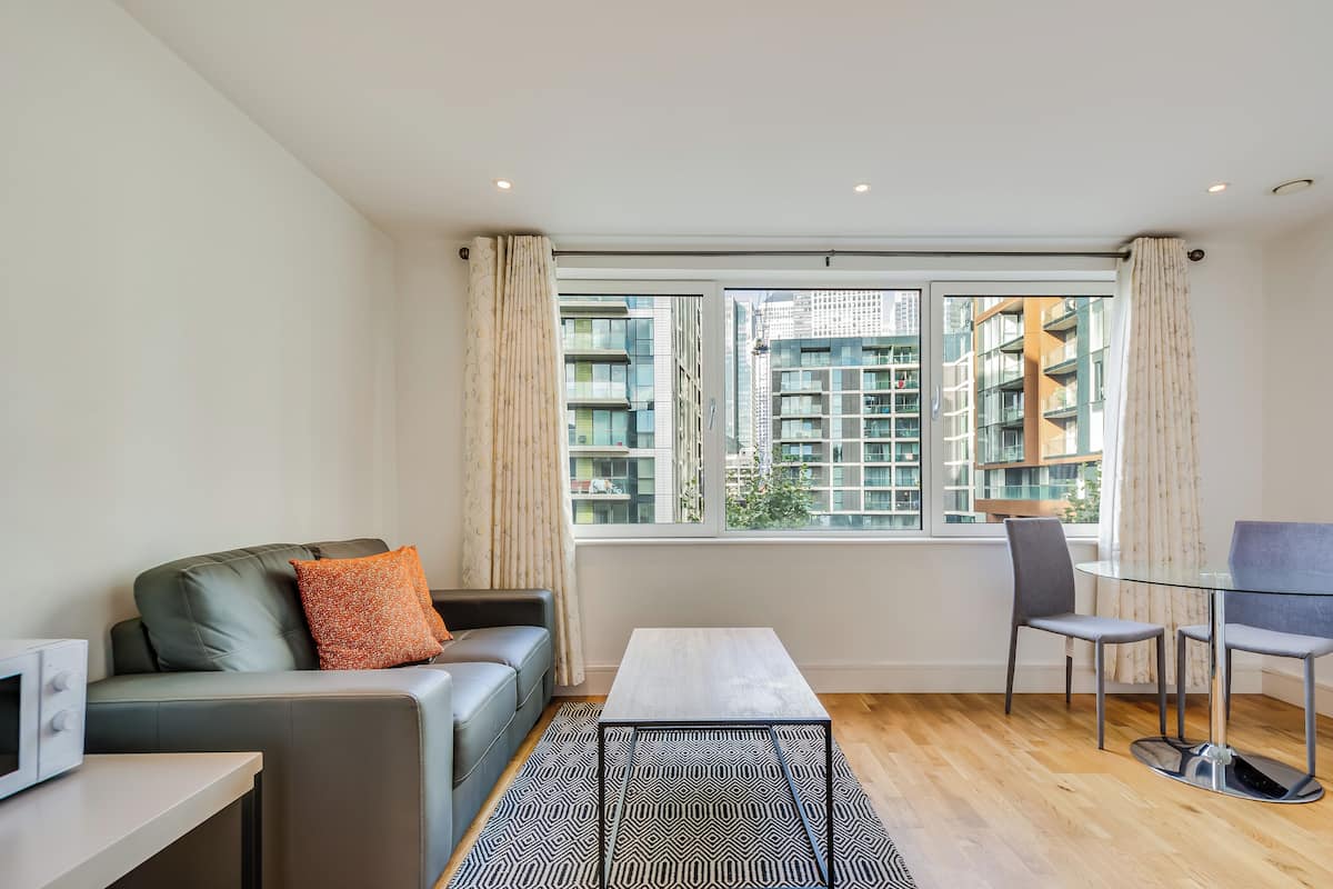 Un salón moderno con un sofá, una mesa de centro de vidrio y vistas a rascacielos a través de amplias ventanas.
