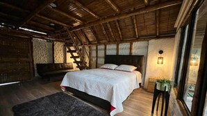 Un dormitorio con una cama grande, suelo de madera, alfombra de piel, una banca, una escalera y una ventana con una planta.
