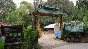 Entrada a un parque con un refugio de madera, un letrero de bienvenida y un cartel informativo sobre los servicios.